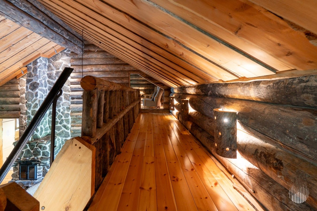 A wooden interior with a sloped ceiling, stone walls, and a wooden staircase.