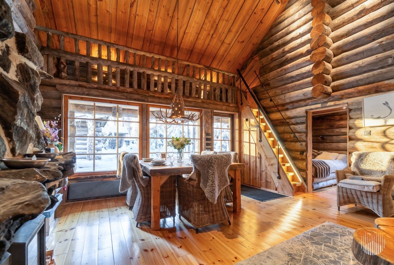 L’intérieur d’une cabane en rondins comprend un coin repas, un escalier et offre une vue sur l’extérieur.