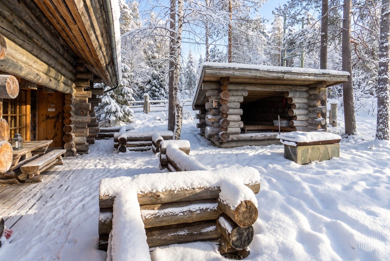 Une cabane en rondins avec une cheminée, des bancs en bois et un sol recouvert de neige.