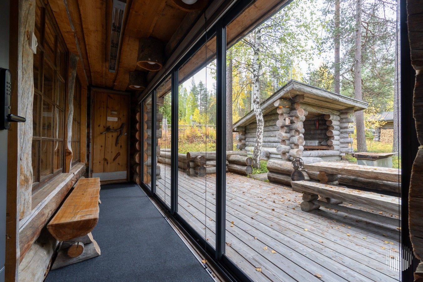 A log cabin interior with a bench, a wooden door, and a view of a log structure outside.
