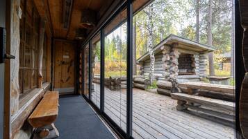 A log cabin interior with a bench, a wooden door, and a view of a log structure outside.