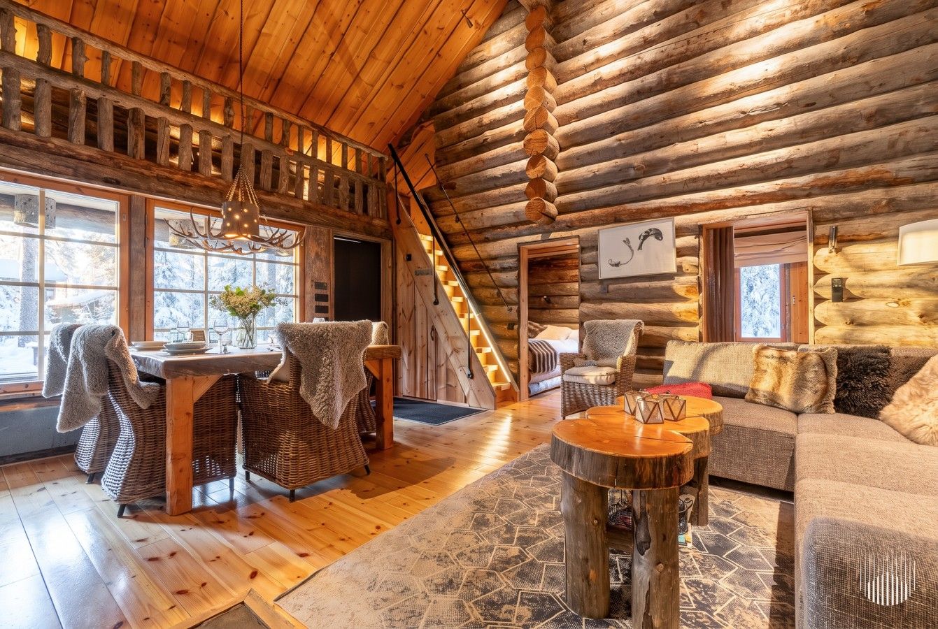 A log cabin interior with a dining area, sofa, and staircase.