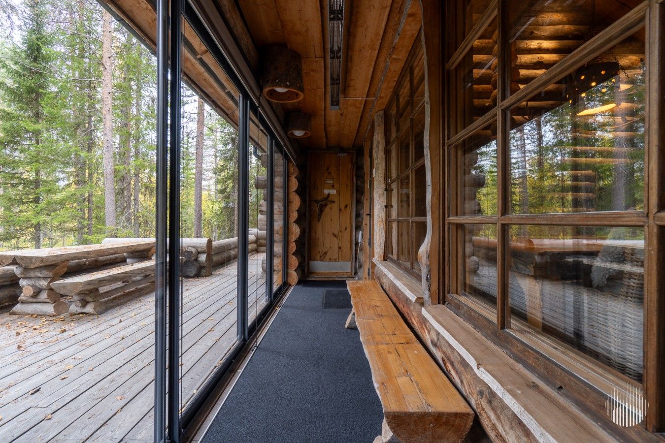 A log cabin interior with large windows, a wooden bench, and a view of the forest.