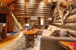 A log cabin interior with a wooden staircase, a sofa set, and a rustic decor style.