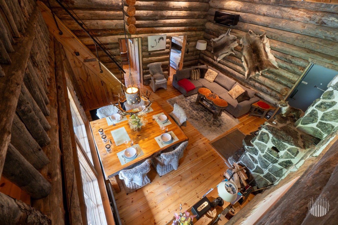 A log cabin interior with a dining area, a stone fireplace, and a mounted animal hide.