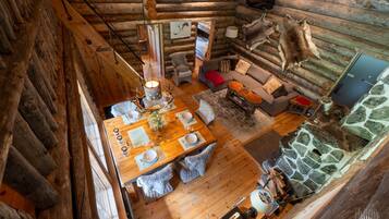 A log cabin interior with a dining area, a stone fireplace, and a mounted animal hide.