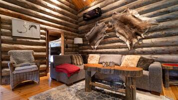 A log cabin interior with a sofa, a chair, a table, and a rug.