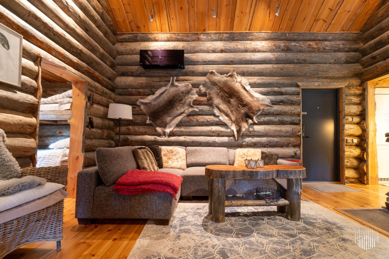 Interior de una cabaña de troncos con un sofá, una mesa y un trofeo de piel de animal colgado.