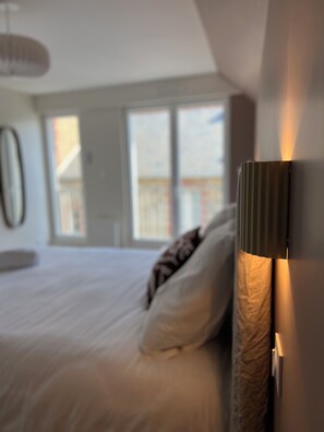 Ein Schlafzimmer mit Bett, Kissen, einer Nachttischlampe und einem Fenster.