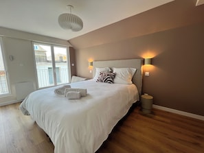 Une chambre à coucher avec un grand lit, un luminaire au plafond, une lampe de chevet et une vue sur l’extérieur grâce à une porte coulissante.