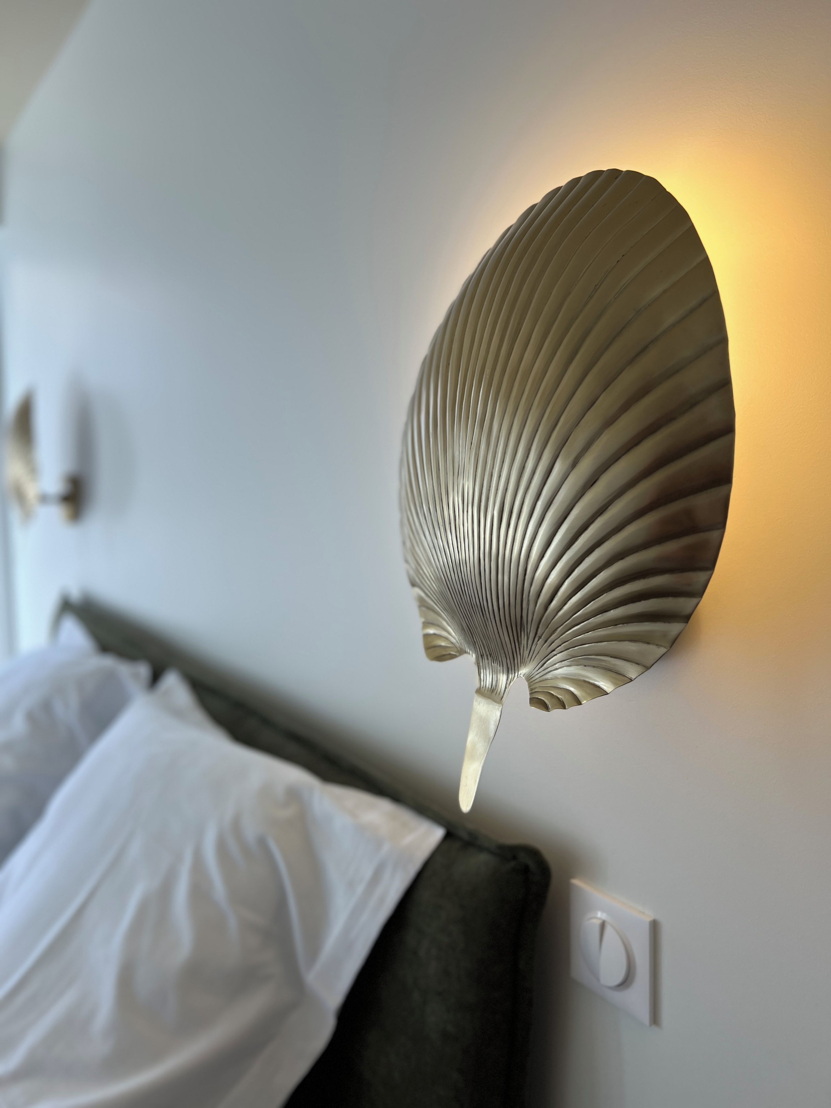 A wall-mounted light fixture with a shell-like design on a white wall.