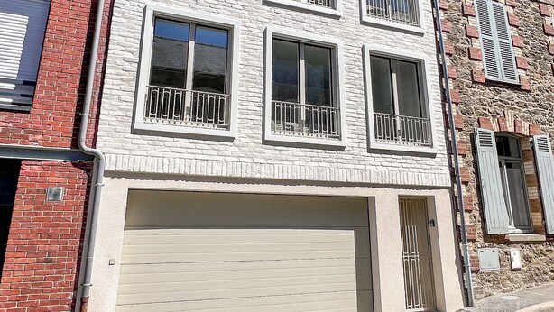 Un edificio de varios pisos con garaje, ventanas amplias y fachada de piedra.