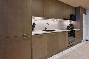 A modern kitchen with wooden cabinets, a black sink, and a built-in oven. - Metsonlinna 204 by Holiday in Lapland (Levi)