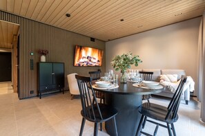 Ein moderner Essbereich mit einem runden Tisch, schwarzen Stühlen und einem an der Wand montierten Fernseher.