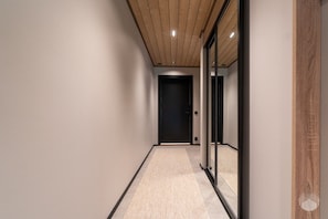 Un pasillo con techo de madera, una puerta negra al final y un separador de vidrio a la derecha.