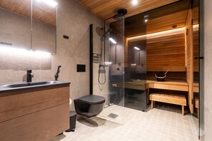 Ein modernes Badezimmer mit einem Holz-Waschtisch, einer schwarzen Toilette, einer gläsernen Dusche und einer Saunabank.