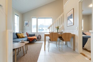 A modern living space with a sofa, coffee table, dining table, and chairs. There is a window with a view of buildings outside. - Cozy and peaceful apartment in Äkäslompolo (Äkäslompolo)