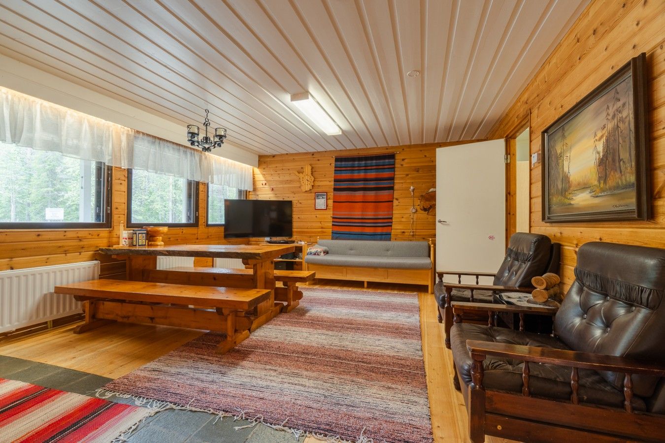 En mysig stuga med träpanel på väggarna, ett tv-appar, en soffa och en öppen spis.