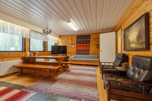 L’intérieur chaleureux d’un chalet, avec un revêtement mural en bois, un téléviseur, un canapé et une cheminée.
