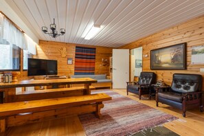 A cozy cabin interior with wooden walls, a television, a fireplace, and a dining area.