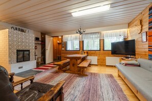 A cozy cabin interior with a fireplace, wooden furniture, a television, and large windows.
