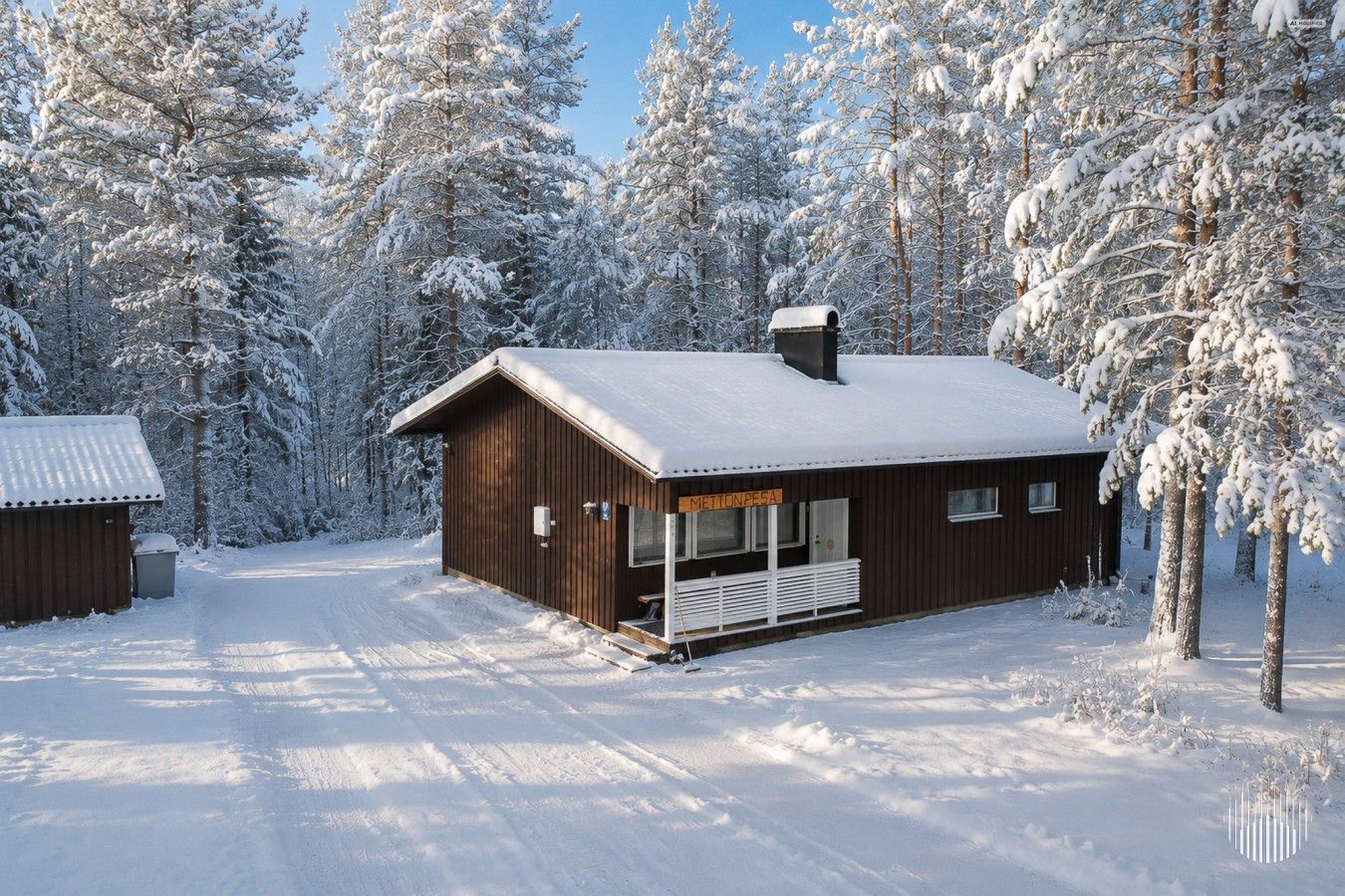 En stuga av trä med en veranda, omgiven av snötäckta träd.
