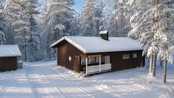 En stuga av trä med en veranda, omgiven av snötäckta träd.