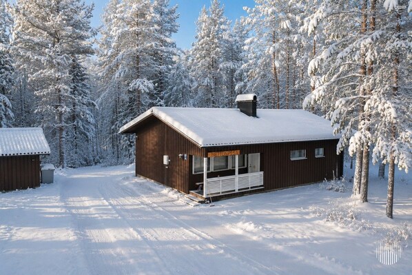 A wooden cabin with a porch, surrounded by snow-covered trees.