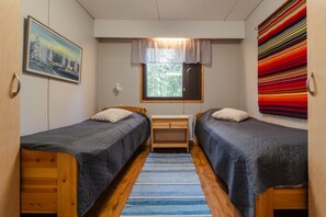 A room with two single beds, a desk, a window with curtains, and a colorful wall hanging.