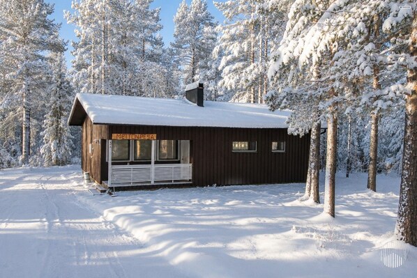 A wooden cabin with a sign reading 'METTON.PESA' in a snowy forest.