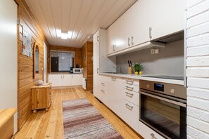 A compact kitchen with wooden walls, a microwave, a stove, and a sink.