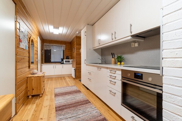 A compact kitchen with wooden walls, a microwave, a stove, and a sink.