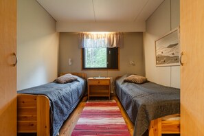 A room with two beds, a desk, and a window with a view of trees.