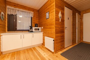 A wooden cabin interior with a kitchenette, a door, and a window with a lace curtain.