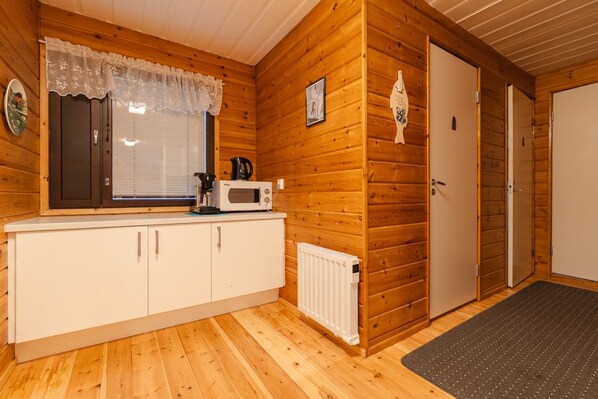 A wooden cabin interior with a kitchenette, a door, and a window with a lace curtain.