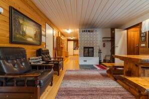 A log cabin interior with a fireplace, leather seating, and a dining area.
