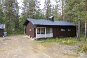 A small, single-story cabin with a dark brown exterior and a sloped roof, surrounded by a forested area.