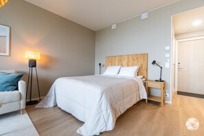 A bedroom with a bed, bedside table, lamp, and a door.