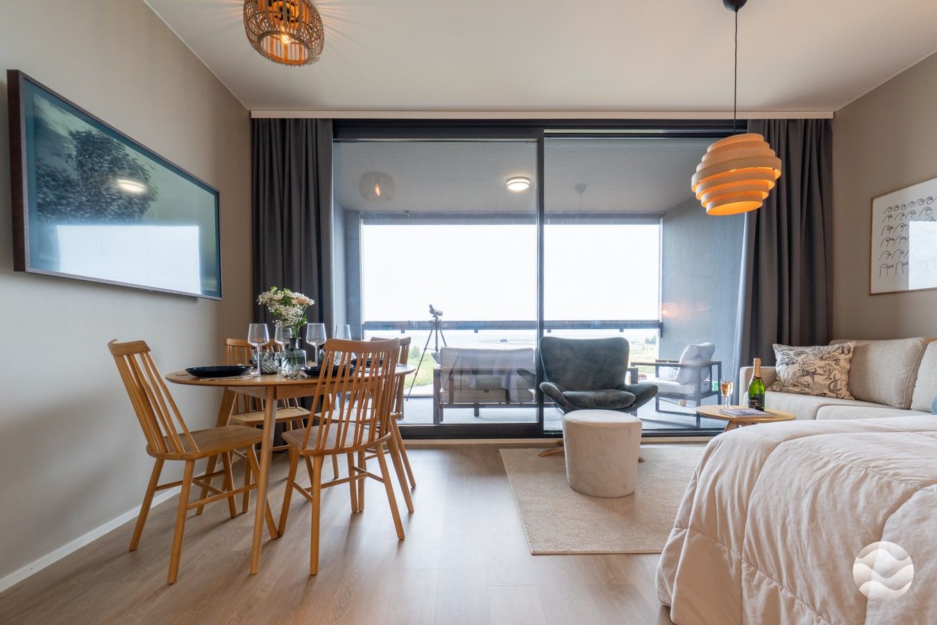 Moderni hotellihuone, jossa on ruokailutila, sohva, sänky ja parveke, jolta on näkymä.