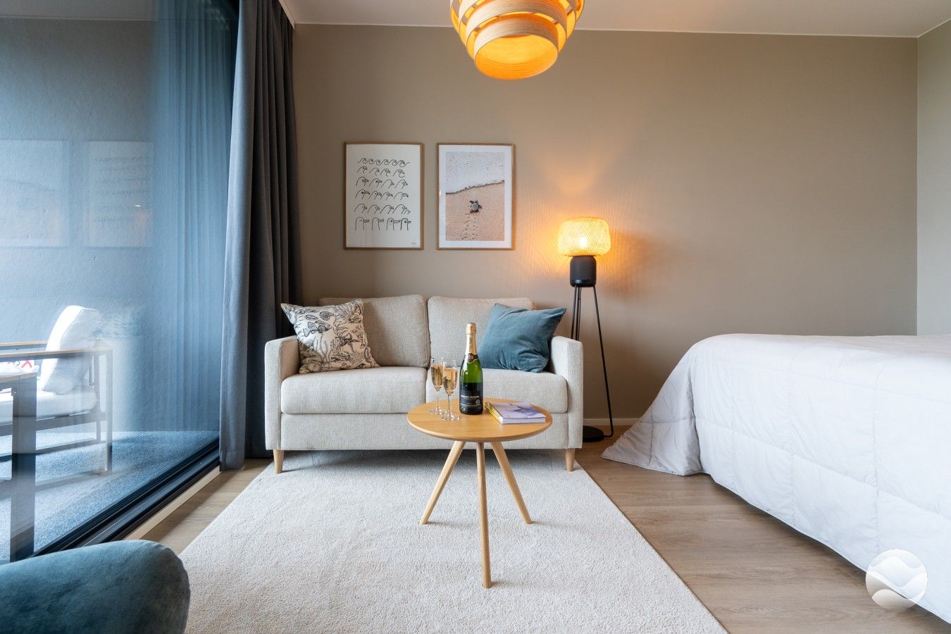 Une chambre d’hôtel avec un canapé, une petite table ronde sur laquelle se trouvent une bouteille et des verres, une lampe et un lit.