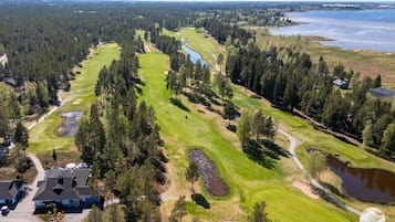 Ein Golfplatz mit Teich, umgeben von dichtem Wald und einigen Gebäuden.
