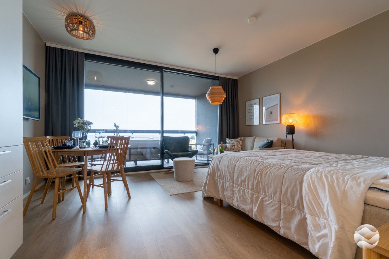 Et moderne hotelværelse med en stor seng, et spisebord med stole, en balkon med udsigt og et stort vindue.