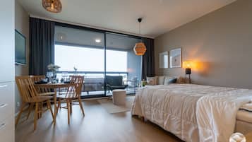 Et moderne hotelværelse med en stor seng, et spisebord med stole, en balkon med udsigt og et stort vindue.
