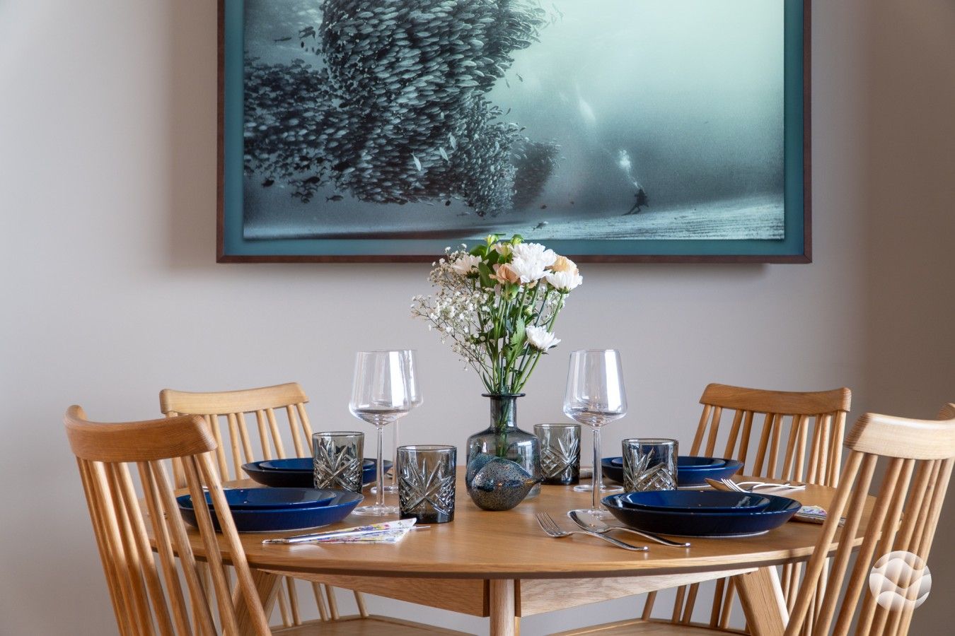A dining table set with blue plates, clear glasses, and a vase with white flowers.