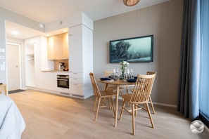 A modern kitchen with white cabinetry, a dining area with a round table and wooden chairs, and a large window with curtains. - Marinan Portin Kapteeni A 39 (Kalajoki)