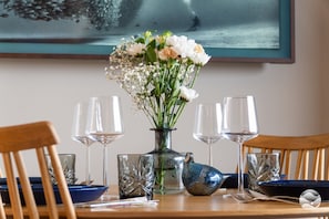 A dining table with a vase of flowers, four wine glasses, and a blue ceramic pitcher.
