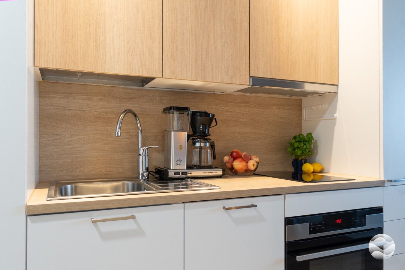 Eine moderne Küche mit Kaffeemaschine, Obstschale und digitaler Uhr.