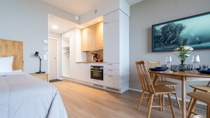 Et moderne hotelværelse med seng, spiseplads med bord og stole, køkken og et stort vindue.