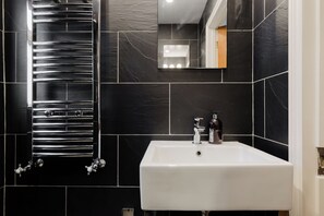 Ein Badezimmer mit einem weißen Waschbecken, schwarzen Fliesenwänden und einem chromfarbenen Handtuchhalter.