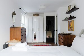 Ein Schlafzimmer mit Bett, Kommode, Kleiderschrank, einem Regal mit Büchern und einem Gemälde.
